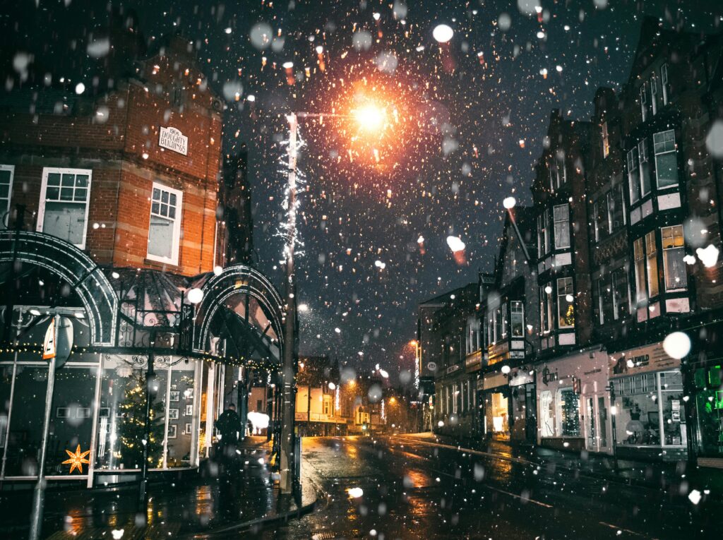 Magical night scene with snow falling on a lit urban street, capturing winter charm.